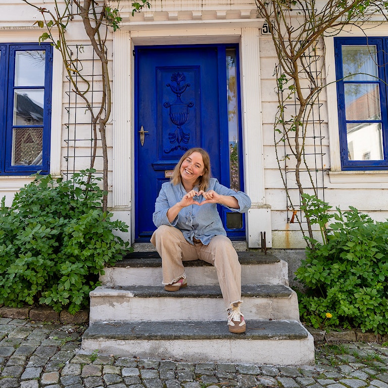 Bilde av Charlotte Nybråten foran et hvitt Bergenshus