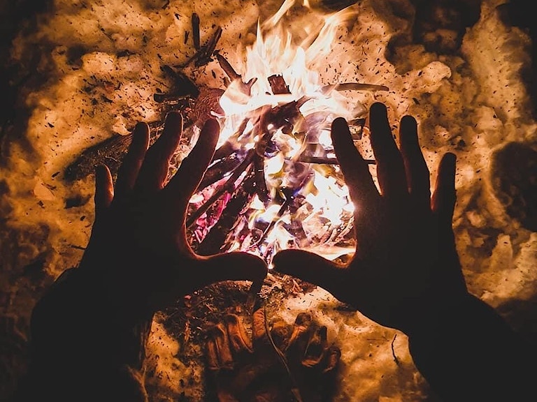 To hender som varmer seg over bålet