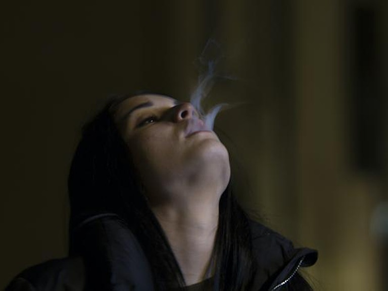 En kvinne blåser røyk ut i luften.