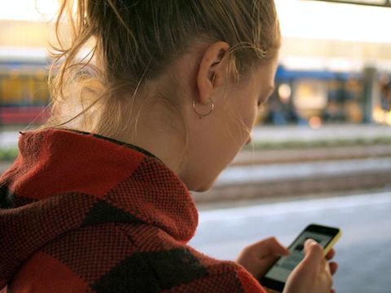 En jente står på en holdeplass og venter på toget. Hun sjekker mobiltelefonen. (Foto: Daria Nepriakhina via unsplash)