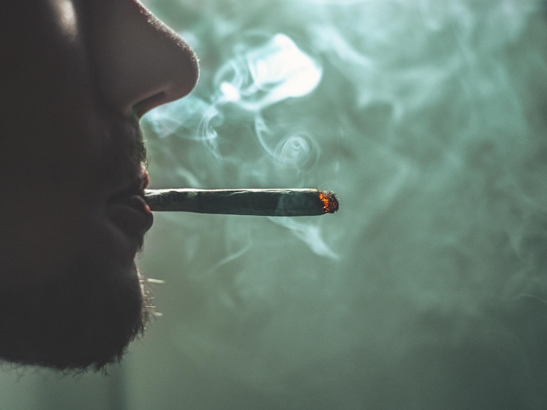 Nærbilde av en mann som røyker en joint. Vi ser bare mannens nese, munn og hake. Rundt ham er det røyk.