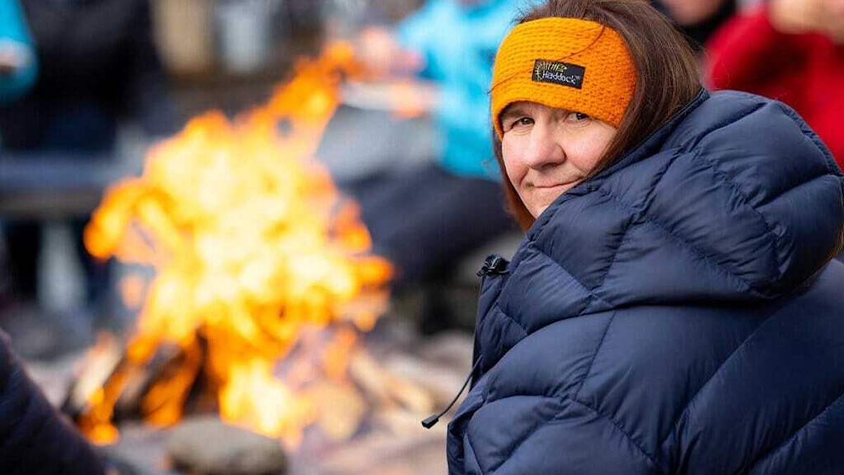 Portrettfotografi av KORUS midt-rådgiver Sigrid Rohde. Hun sitter ved et bål ikledd varm jakke og pannebånd.