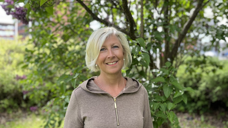 Portrett av Hilde Jeanette Loberg fra KORUS. Hun står ute foran et tre. Det er vår, sola skinner og hun smiler. (Foto: Bjorn Sodeland)