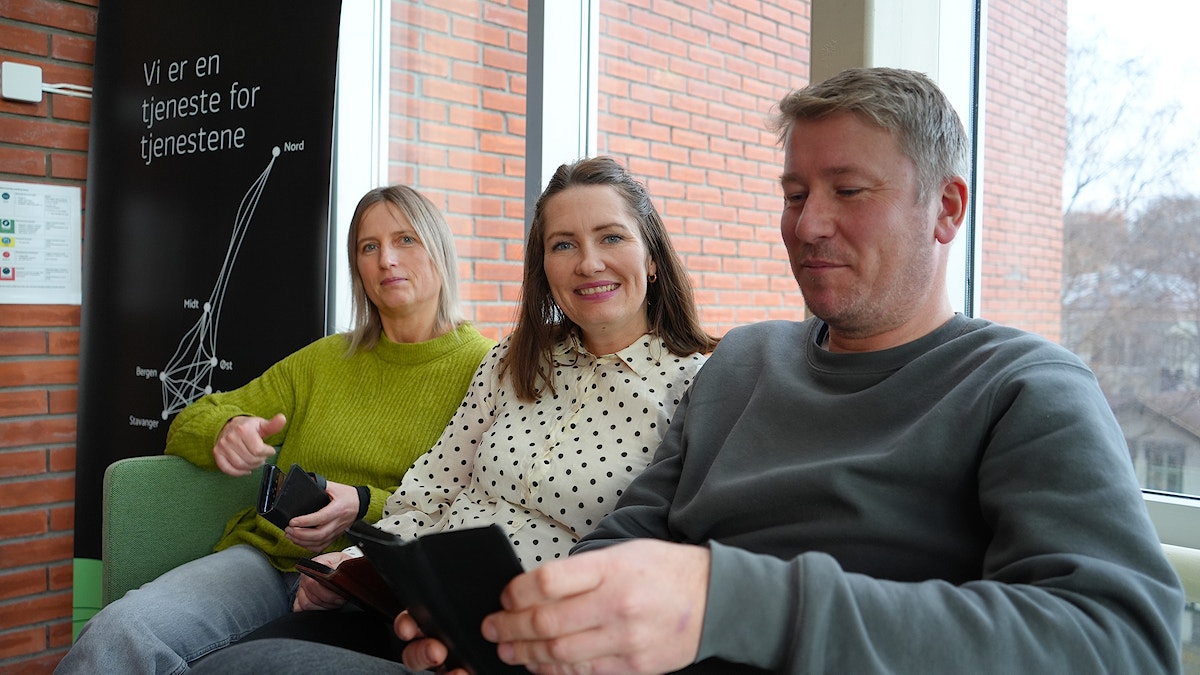 Rosanne Kristiansen, Ingvild Vardheim og Asle Bentsen fra KORUS sør sitter på en sofa med hver sin mobiltelefon. Stemningen er god.