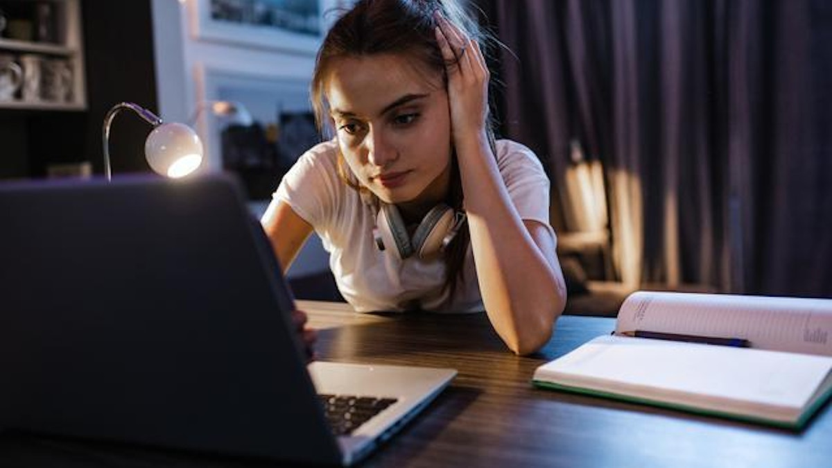 En ung kvinne sitter ved PC-en. Det er skumring ute og hun studerer. Foto: Istock