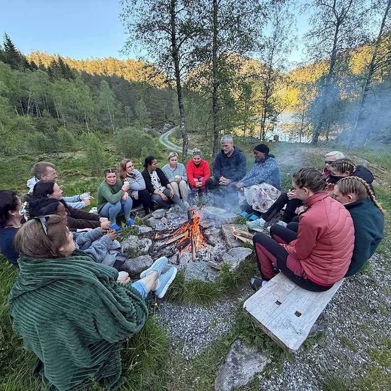 En gruppe mennesker som sitter rundt et bål og snakker sammen.