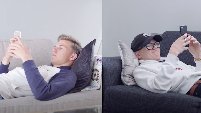 To unge gutter ligger på hver sin sofa og kikker på mobiltelefonen sin.