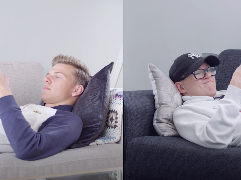 To unge gutter ligger på hver sin sofa og kikker på mobiltelefonen sin.