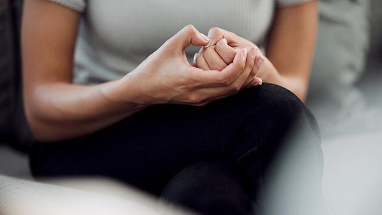 En kvinne sitter med hendende sammen og klør seg med tommelen på negleroten. Hun virker nervøs. (Foto: Istock)