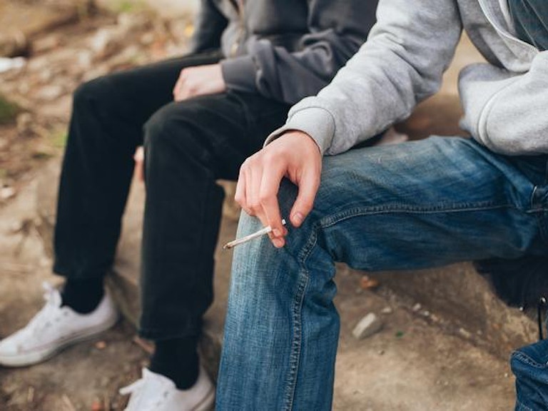 To ungdommer sitter på en trapp og deler en joint.