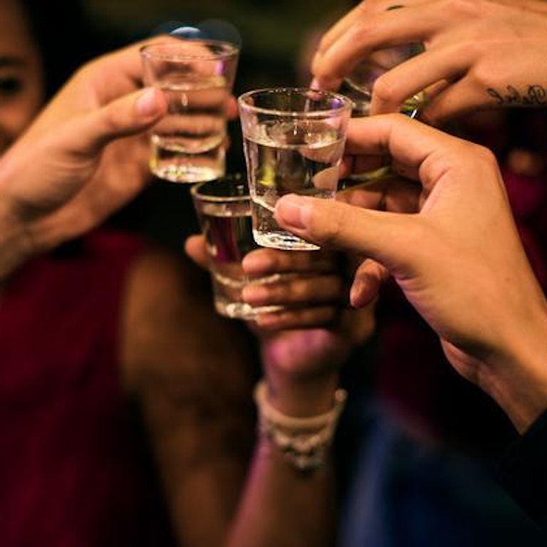 En gruppe mennesker står samlet i ring og skåler med shotsglass. Stemningen er god. (Foto: Istock)