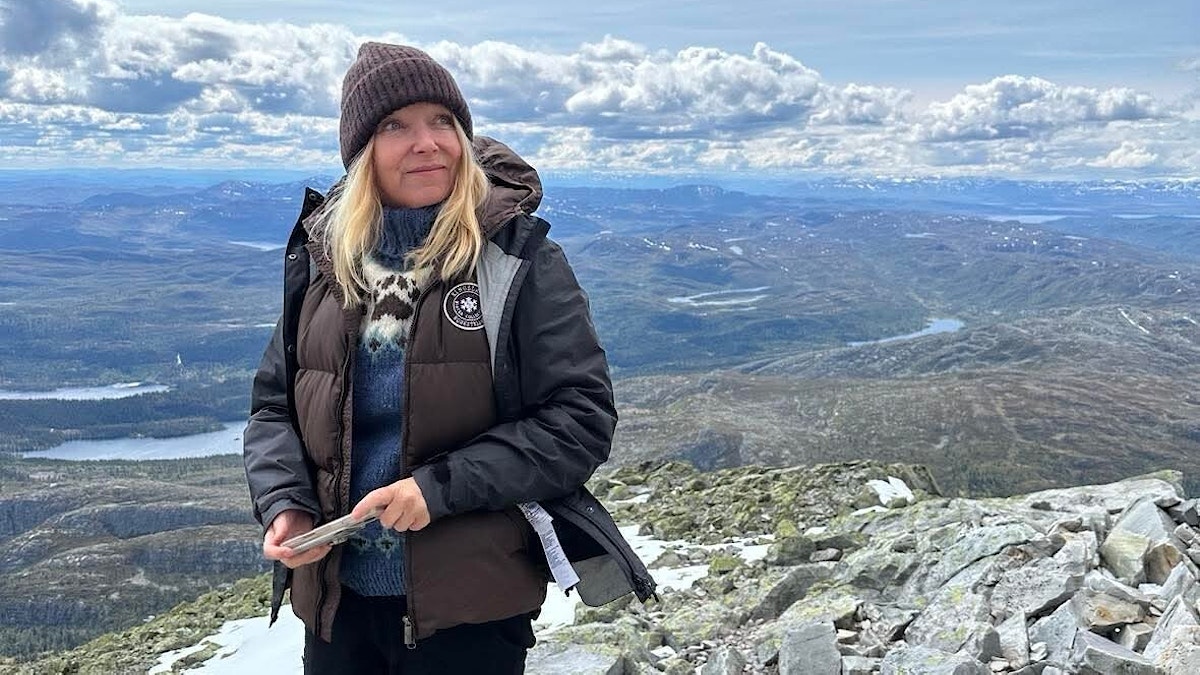 Yvonne liker turer i skog og mark. Her er hun på tur i fjellet. Himmelen er klar og blå med noen skyer, og Yvonne har på seg boblejakke, lue og skjerf.