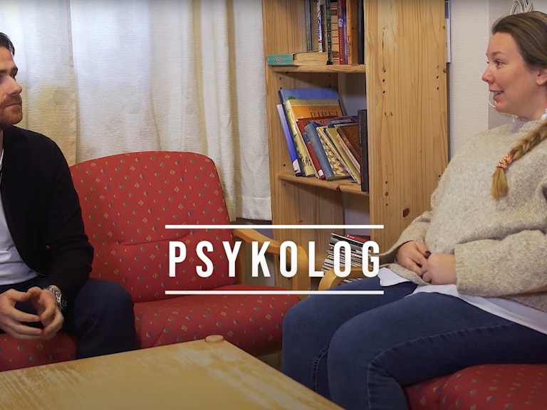 Bildet viser en kvinne og en mann som sitter i hver sin sofa. De ser på hverandre, og det ser ut som om de er midt i en samtale. Midt på skjermen står det skrevet «Psykolog» med store bokstaver.