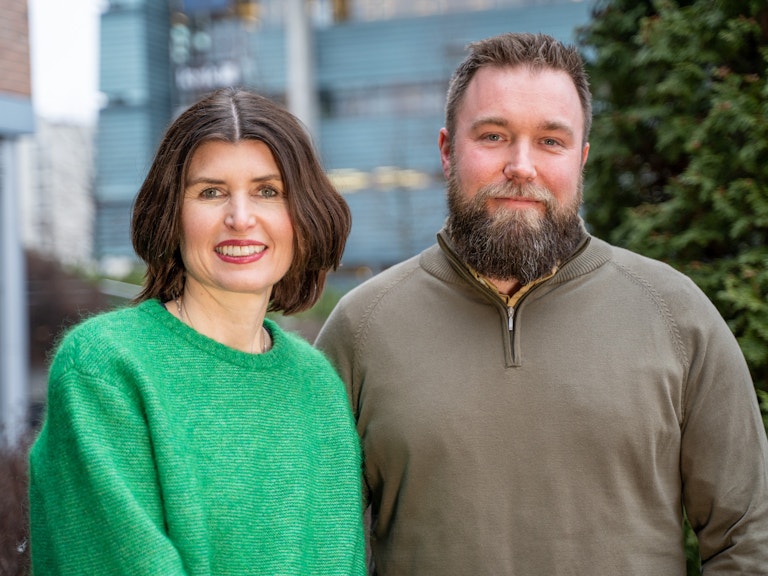 Dame med kort hår og grønn genser står ved siden av mann med skjegg og brun genser