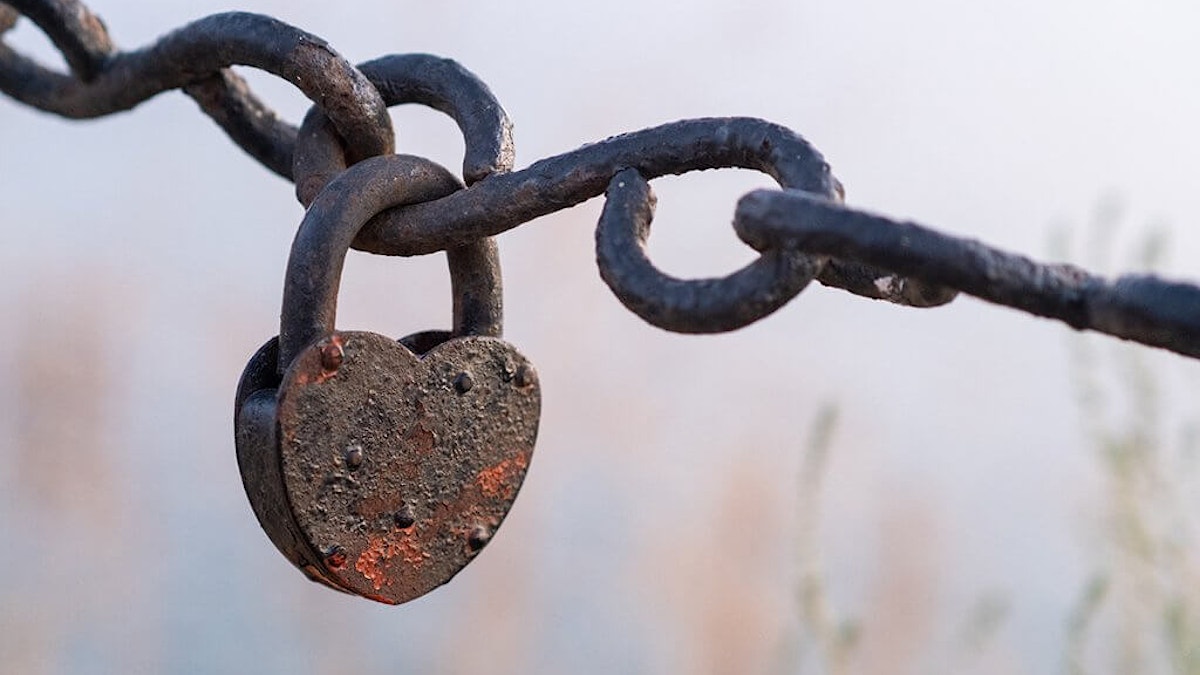 En rusten hengelås henger i en rusten kjetting. Låsen er formet som et hjerte. Foto Shutterstock