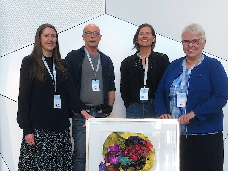 Bildet viser fire smilende representanter fra Suldal kommune etter at de vant Kommunerusprisen. Premien, et maleri, står på gulvet foran dem.