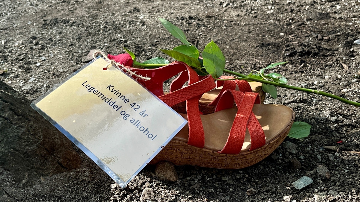 Bildet viser et par kvinnesandaler på grusen. Oppå sandalene ligger en rose og en liten plakat hvor det står «Kvinne 42 år, legemiddel og alkohol». Bildet er tatt i forbindelse med markeringen av Verdens overdosedag. Foto: Tone Helene Oskarsen