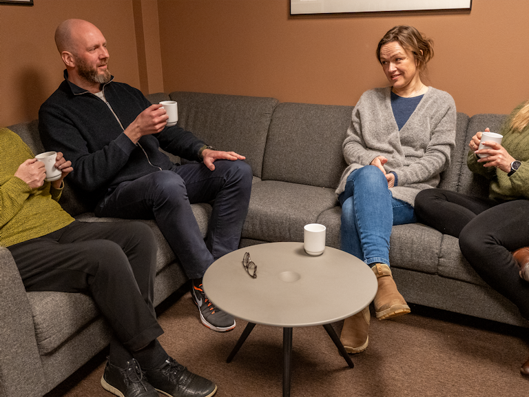 Bilde av fire medarbeidere i KORUS Bergen som sitter i sofaen med en kopp kaffe