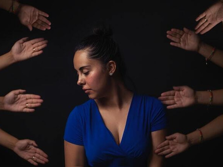 Kvinne med lukkede øyne, rundt henne en masse ustrakte hender