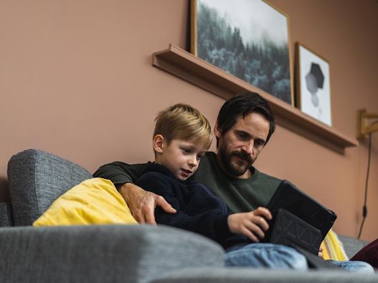 En far sitter med barnet sitt i armkroken og leser en bok i sofaen. Det ser ut som de koser seg. (Foto: Jonas Ingstad)