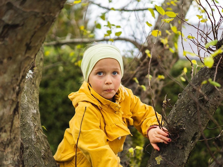 Jente med gul jakke klatrer i et tre