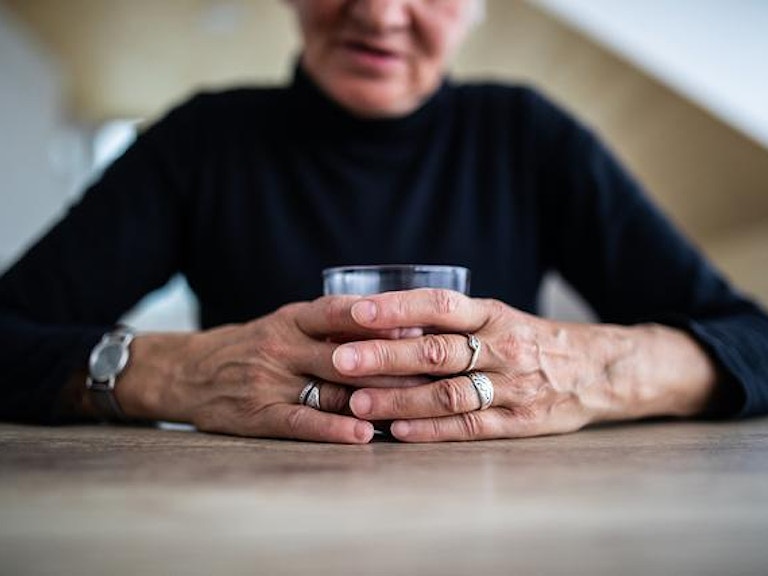 Eldre kvinne sitter med et vannglass i hendene ved et bord.