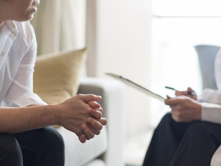 To personer sitter overfor hverandre i en sofa. Den ene holder papir og penn. (Foto: Istock)