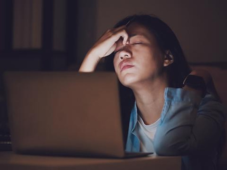 En kvinne sitter foran en PC. Hun virker sliten. (Foto: Istock)