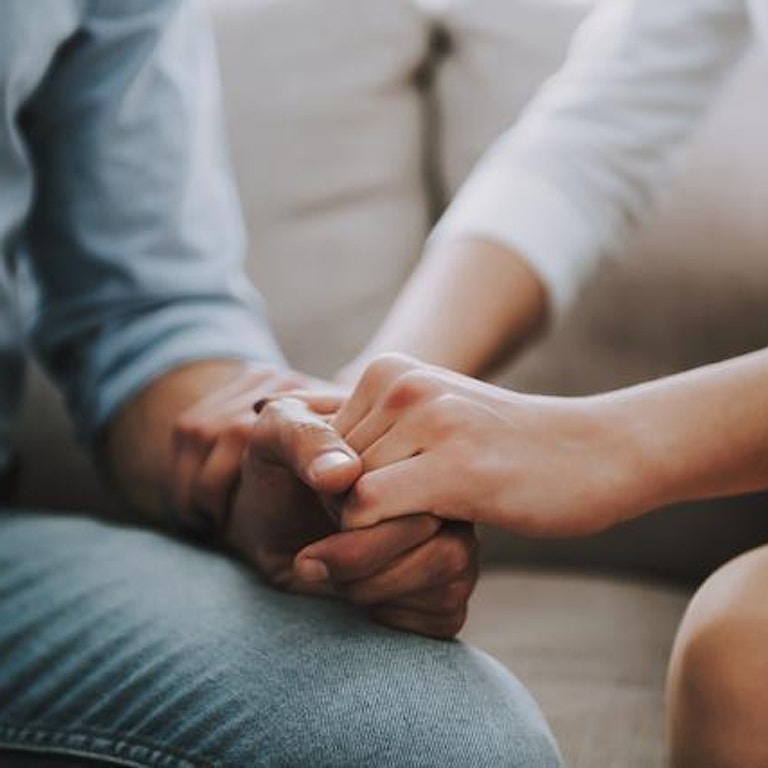 Et par sitter tett inntil hverandre og holder hender. De virker bekymret. (Foto: Istock)