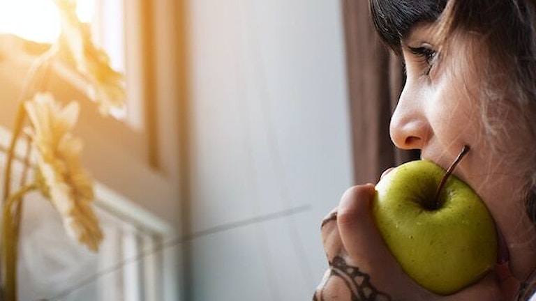 kvinne spiser eple mens hun ser ut av et vindu